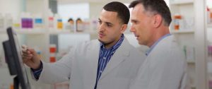 Two pharmacists reviewing a tablet in a pharmacy, discussing their careers.
