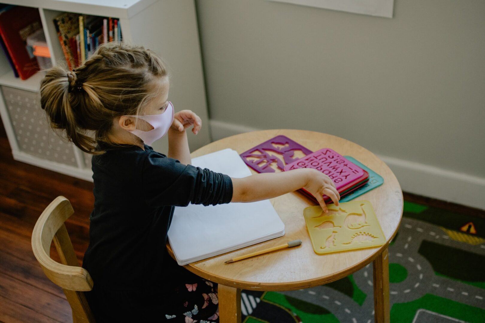 A little girl sitting at a table with a mask on her face, depicting her concern for mental health.