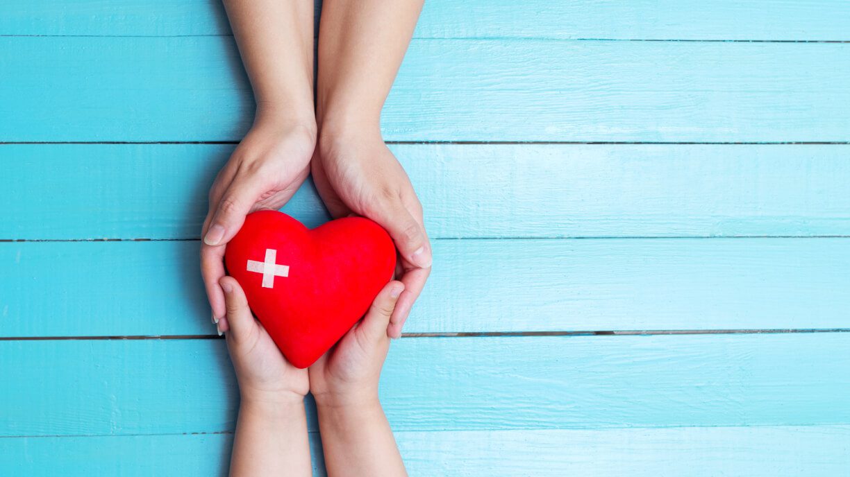 Two hands holding a red heart on a blue wooden background, symbolizing the power of love and compassion in effective management software.