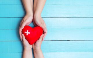 Two hands holding a red heart on a blue wooden background, symbolizing the power of love and compassion in effective management software.