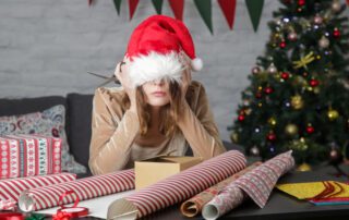 A woman in a santa hat sitting at a table with christmas presents, organizing them using management software.