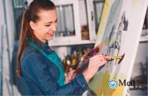 A woman is using management software to track her progress while painting on an easel in an art studio.