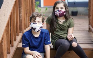 Two children sitting on steps wearing face masks to protect their mental health.