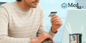 A man holding a credit card in front of a laptop.