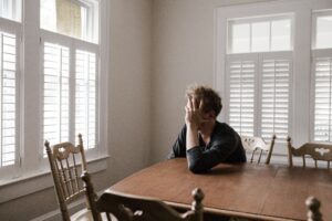 A man sitting at a table in front of a window, contemplating his men's mental health.