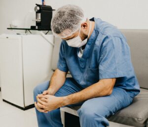 A man in scrubs sitting on a bench in a hospital, showcasing healthcare workers stress.