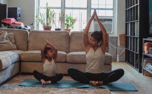 A mother and daughter engaging in yoga poses in a living room, promoting children's mental health.