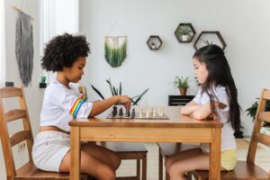 Two girls engaging in a game of chess in the living room, emphasizing the importance of children's mental health.