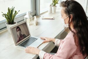 A woman is using a laptop for a telehealth video call.