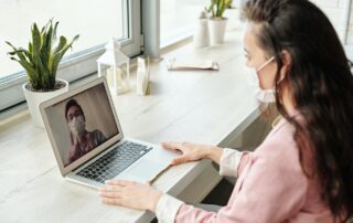 A woman is using a laptop for a telehealth video call.