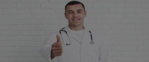 A doctor giving a thumbs up in front of a brick wall.